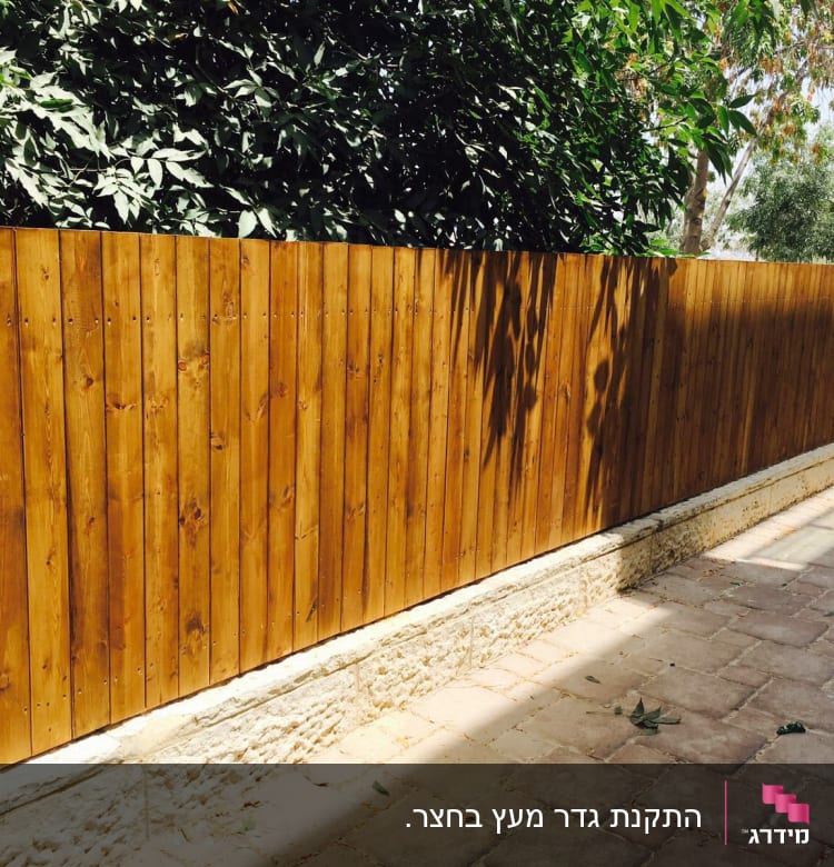 גדר עץ חומה לצד שביל מרוצף בגינה